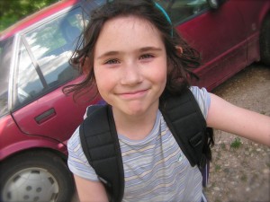 Kid smiling in front of car with book bag on