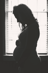 Pregnant woman silhouetted in front of window. Black and white.