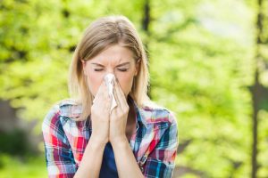 Woman suffering from allergies blows her nose outdoors