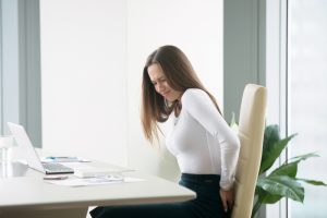 Profile portrait of an irritated young businesswoman woman at the office, feeling her back tired after working at laptop, uncomfortable chair, feeling severe back ache, difficulty sitting