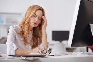 Woman at computer with glasses off rubbing head because of headache