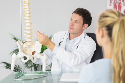 Doctor explains back pain and chiropractic care with a model of a spine suspended on a rod.